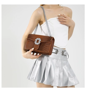 Detail of brown crocodile pattern handbag with rhinestone buckle and silver chain strap