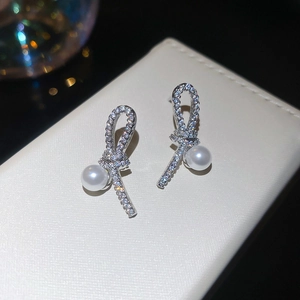 Macro view of silver knotted earrings with sparkling zircon pave and a glossy white pearl