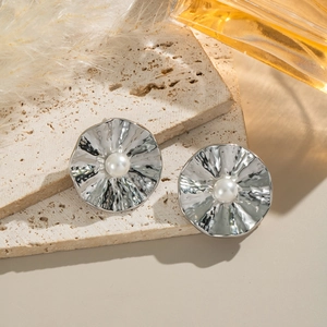 Close-up of silver textured ruffle earrings with pearl on a natural stone surface