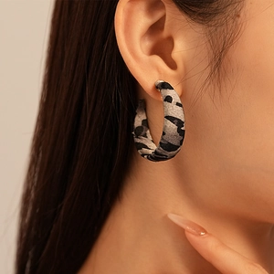 Detailed view of grey leopard print fabric hoop earrings worn on a female model