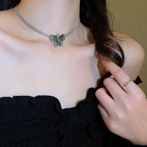 Close-up of a silver butterfly necklace with green crystal and matching ring on a model