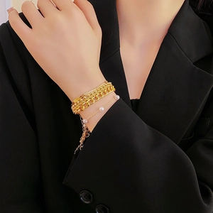 Close-up of layered gold pearl bracelets worn over a black sleeve for a chic look