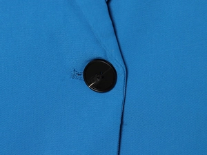 Détail d'un bouton noir et de la texture du tissu sur un ensemble blazer bleu à manches longues