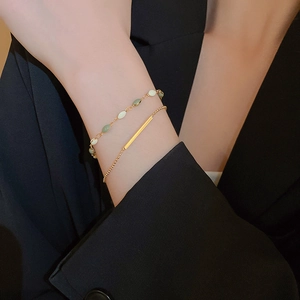Detail of layered gold-plated geometric bracelets featuring green and beige enamel accents