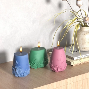 Three Nordic floral embossed candles in blue, green, and pink colors on wood