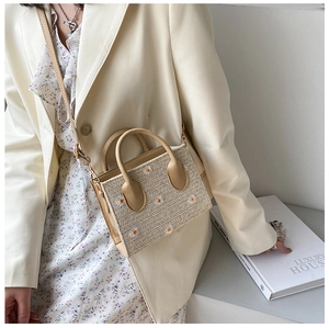 Detail of daisy embroidery on a beige woven crossbody bag with leather handles