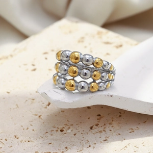 Detail of three-layer beaded knot ring in gold and silver on a beige stone base