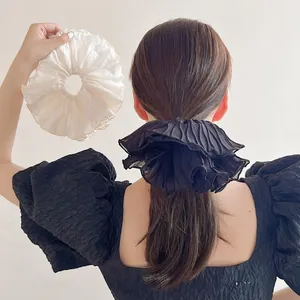 Detail of oversized pleated scrunchies in black and cream fabric on hair and hand
