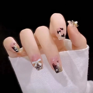 Elegant black and white press-on nails with gold glitter, bows, and heart patterns