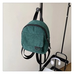 Detailed side view of the dark green corduroy mini backpack on a metal stand