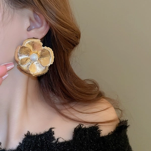 Detail of oversized gold flower earring with textured petals and a central white pearl