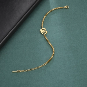 Golden OM yoga symbol pendant box chain anklet for women on a green textured background