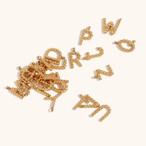 Detailed view of 18K gold plated twisted rope texture alphabet pendants on beige surface