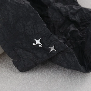 Macro detail of asymmetric silver star earrings on a textured black paper background