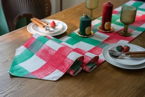 Detail of red and green plaid table runner with stitching on dark wood table