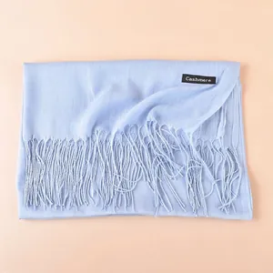 Detail of light blue cashmere scarf with elegant tassels and stitched logo tag