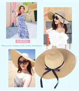 Detail of wide brim straw sun hat featuring a black ribbon bow and natural woven texture