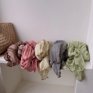 Detail of pleated silk scarves in earth tones hanging beside a woven handbag