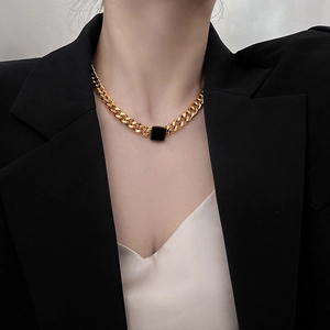 Close-up of golden chunky chain necklace with black square pendant on a female model