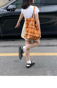 Outdoor shot of a woman carrying a large orange checkered canvas tote bag on her shoulder