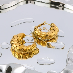Golden twisted croissant hoop earrings on a silver ripple tray with water droplets