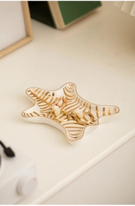 Detailed view of star-shaped ceramic jewelry tray with golden zebra pattern and earrings