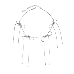 Detailed close-up of silver metal bow pendant with long tassels on a snake bone chain