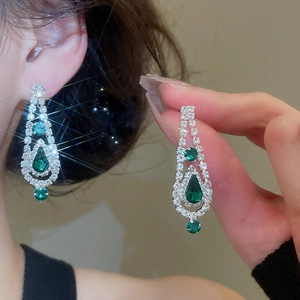 Detail of silver drop earrings featuring green gems and tassels in luxury style