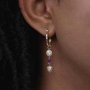 Macro detail of gold hoop earring with tiered purple crystal and geometric pendants