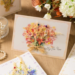 Handmade thank you card with dried orange lilies and envelope on a rustic wooden table