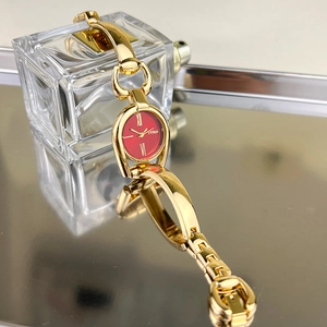 Close-up of a vintage-style gold horsebit bracelet watch with a striking red dial face