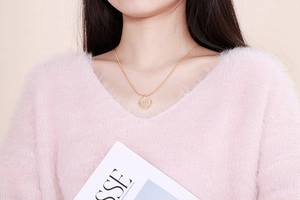 Close-up of golden zodiac necklace with m symbol pendant on pink mohair sweater