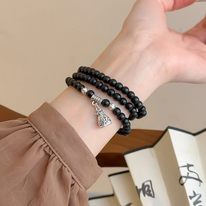 Macro detail of multi-layer beaded bracelet featuring silver money bag charm with Fu symbol