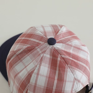 Top view detail of red and white plaid fabric with navy blue button on a kids baseball cap
