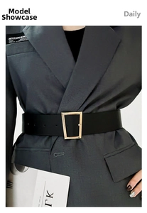 Close-up of a wide black belt with a gold geometric metal buckle over a grey blazer