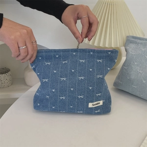 Detail view of denim cosmetic bag with white bow embroidery and zip closure