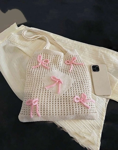 Flat lay of cream crochet tote bag with pink bows showing large capacity next to a phone