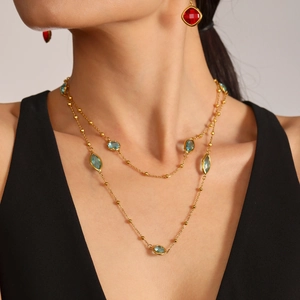 Luxuriöse goldene Doppelkette mit blauen Steinen und roten quadratischen Ohrhängern am Model
