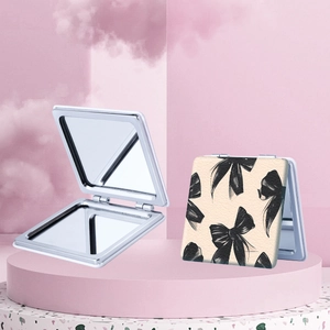 Portable silver folding square makeup mirror set with black bow patterns on pink display