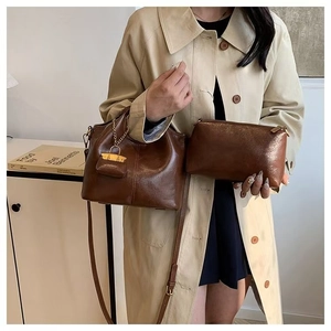 Brown oil wax leather tote bag and clutch set worn by a model in a cozy indoor setting
