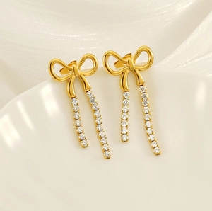 Close-up of golden bow earrings with sparkling rhinestone tassels on white ceramic