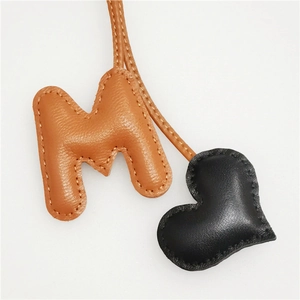 Close-up of brown letter M and black heart leather bag charm with litchi texture