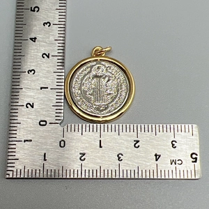 Macro view of round religious medal pendant showing precise size measurement on ruler