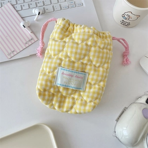 Close-up of heart-quilted camera pouch in yellow plaid with pink drawstring on a desk