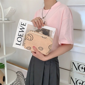 Corduroy makeup bag in beige with black smile print held by a model with a magazine
