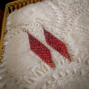 Détail de longues boucles d'oreilles losanges rouges serties de diamants sur de la dentelle
