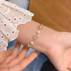 Dettaglio del bracciale dorato con cuori e perle sul polso con pizzo elegante