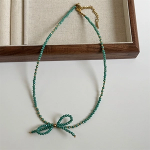 Macro detail of a green faceted bead necklace with a handmade beaded bow and gold clasp