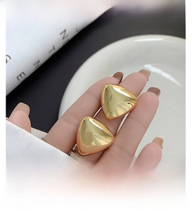 Detailed close-up of polished 18K gold triangle studs with a sleek mirror finish texture