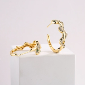 Exaggerated 18K gold snake earrings with clear and green zircons on white pedestal